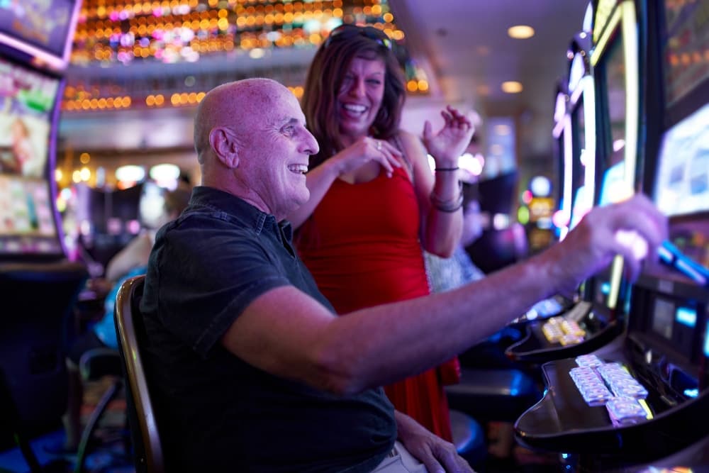 A man and a woman joyfully interact at a casino slot machine.