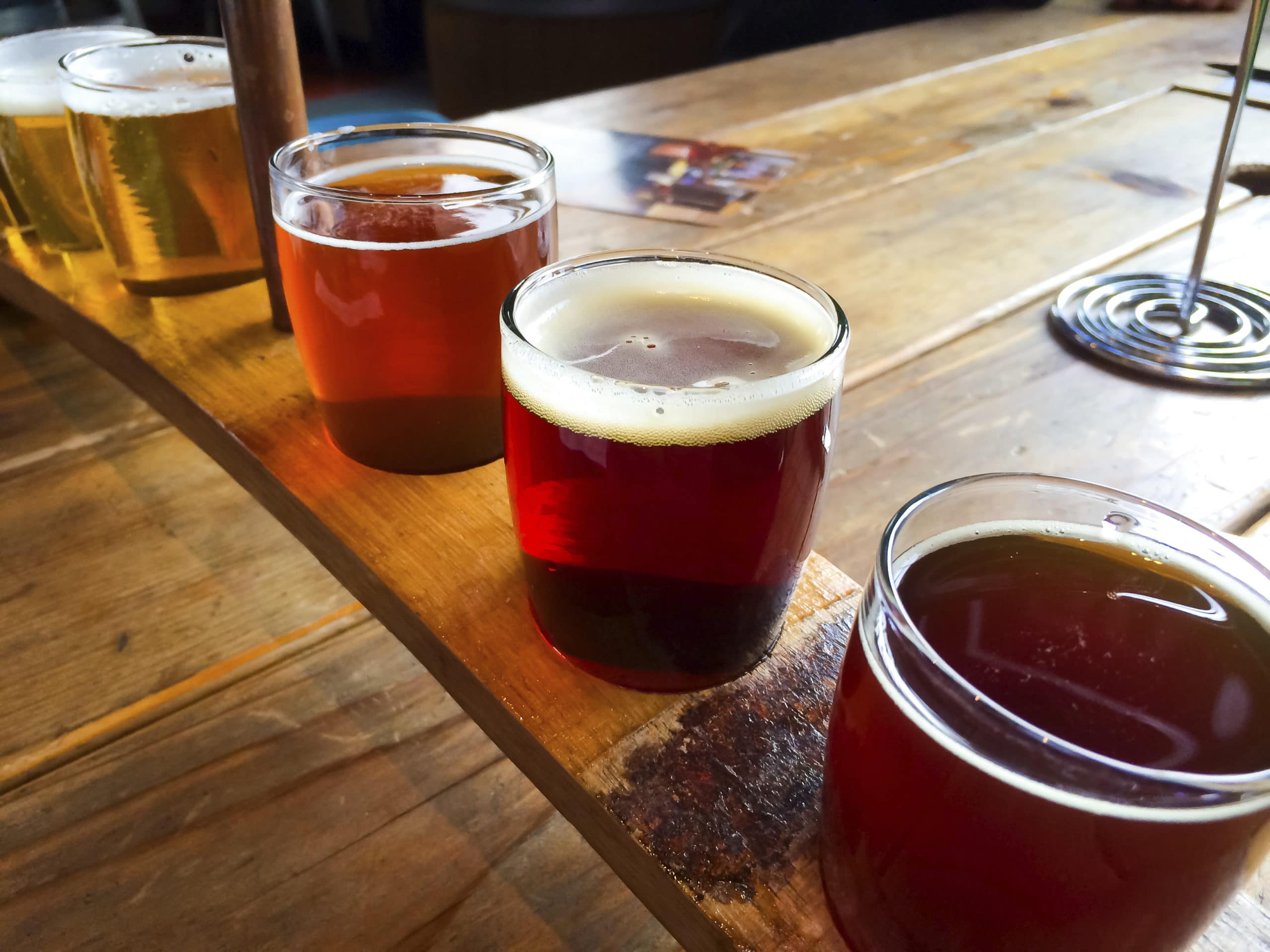 A flight of five craft beer samples arranged on a wooden paddle.