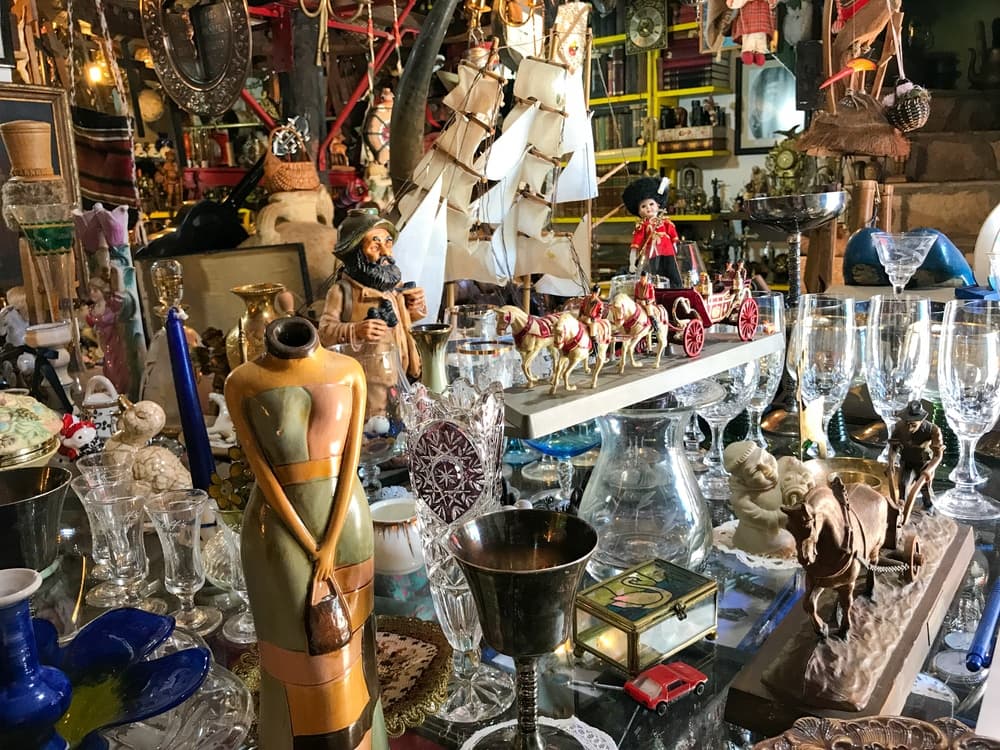 A cluttered display of various antiques and collectibles, including figurines, glassware, and decorative items.