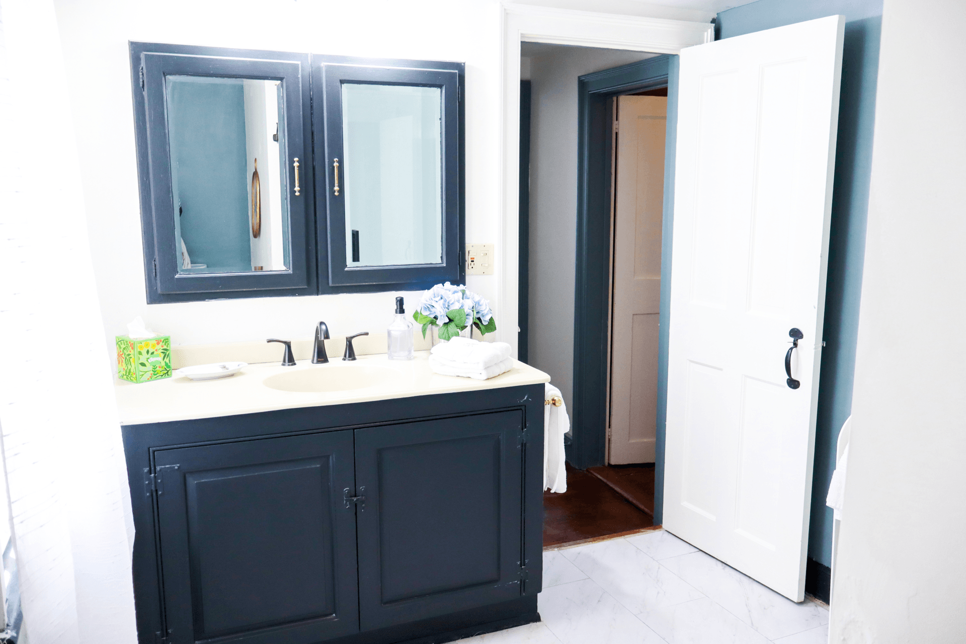 Bright bathroom featuring a black vanity, double mirrors, and an open door leading to a hallway.