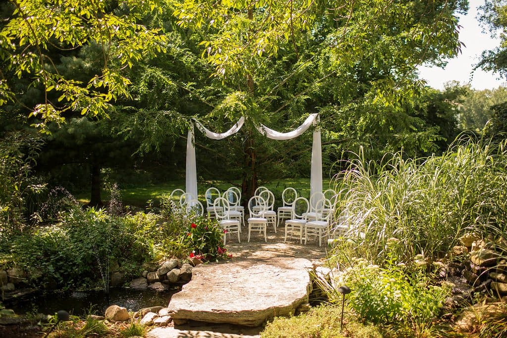 A serene outdoor wedding setup featuring white chairs arranged around a stone path and a floral arch.