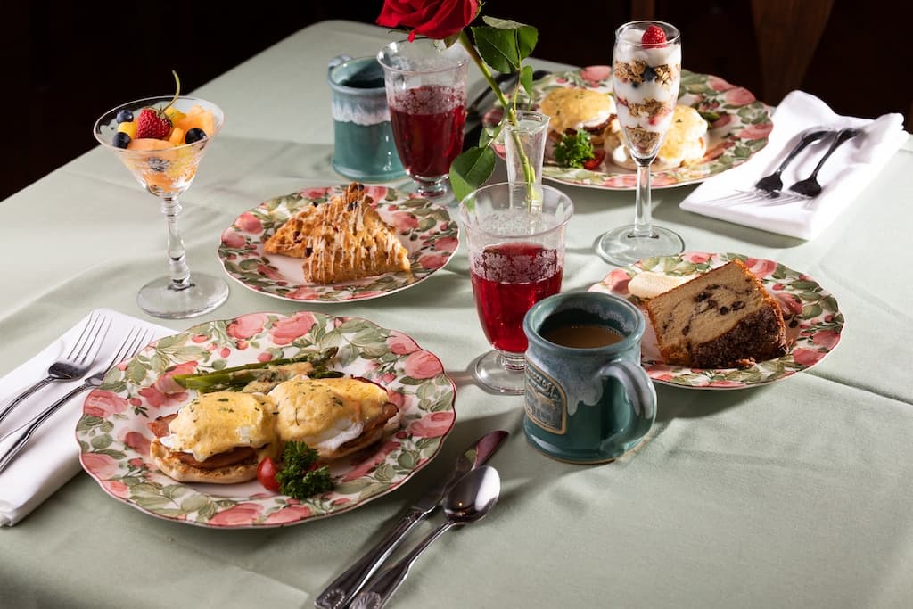 A beautifully arranged table set with plates of gourmet food, desserts, drinks, and a rose centerpiece.