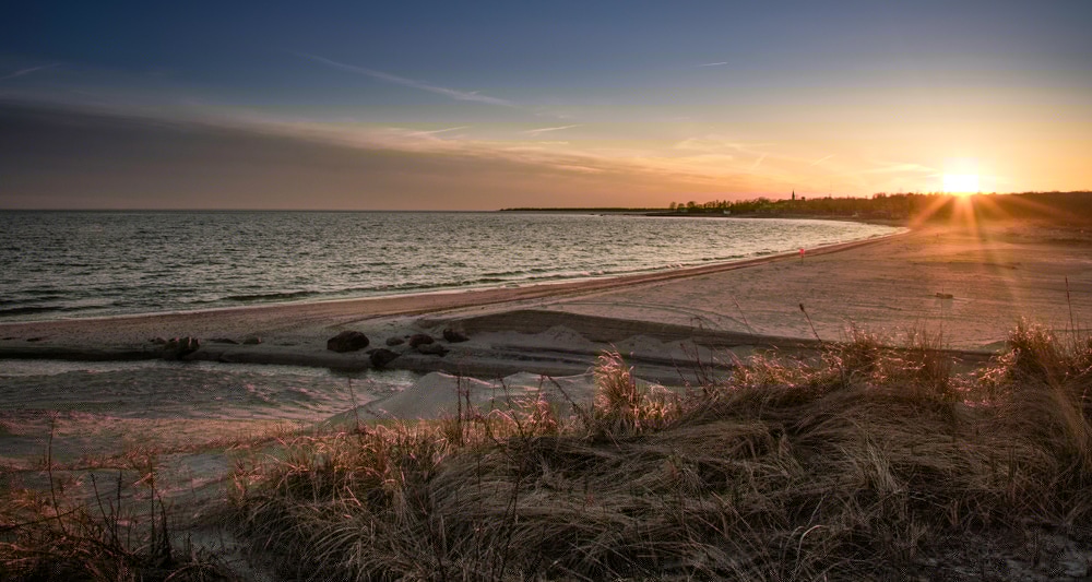 Sunset over a tranquil beach with gentle waves and sandy dunes.