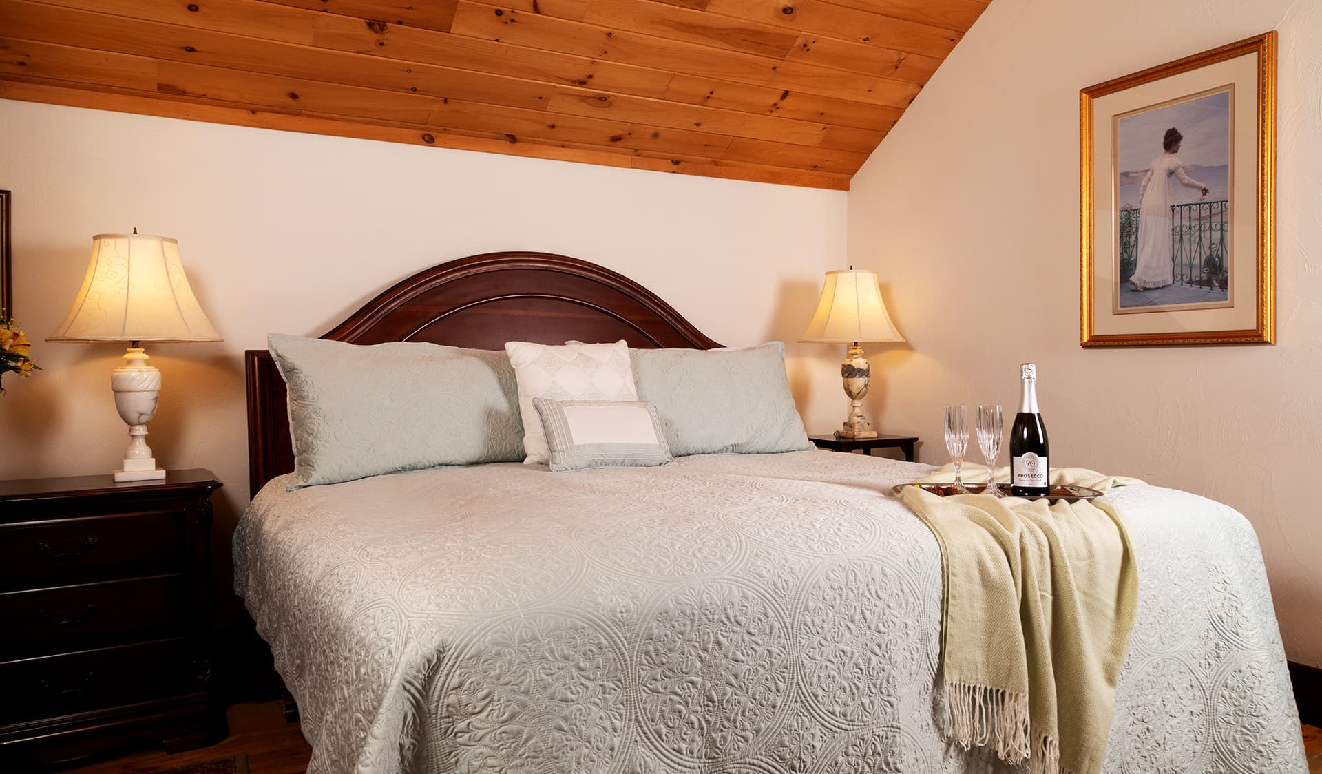 Cozy bedroom with a king-sized bed, soft linens, bedside lamps, and a bottle of champagne on a side table.