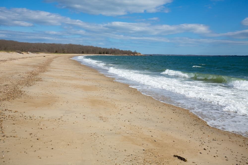 A sandy beach curves along a tranquil ocean under a partly cloudy sky.