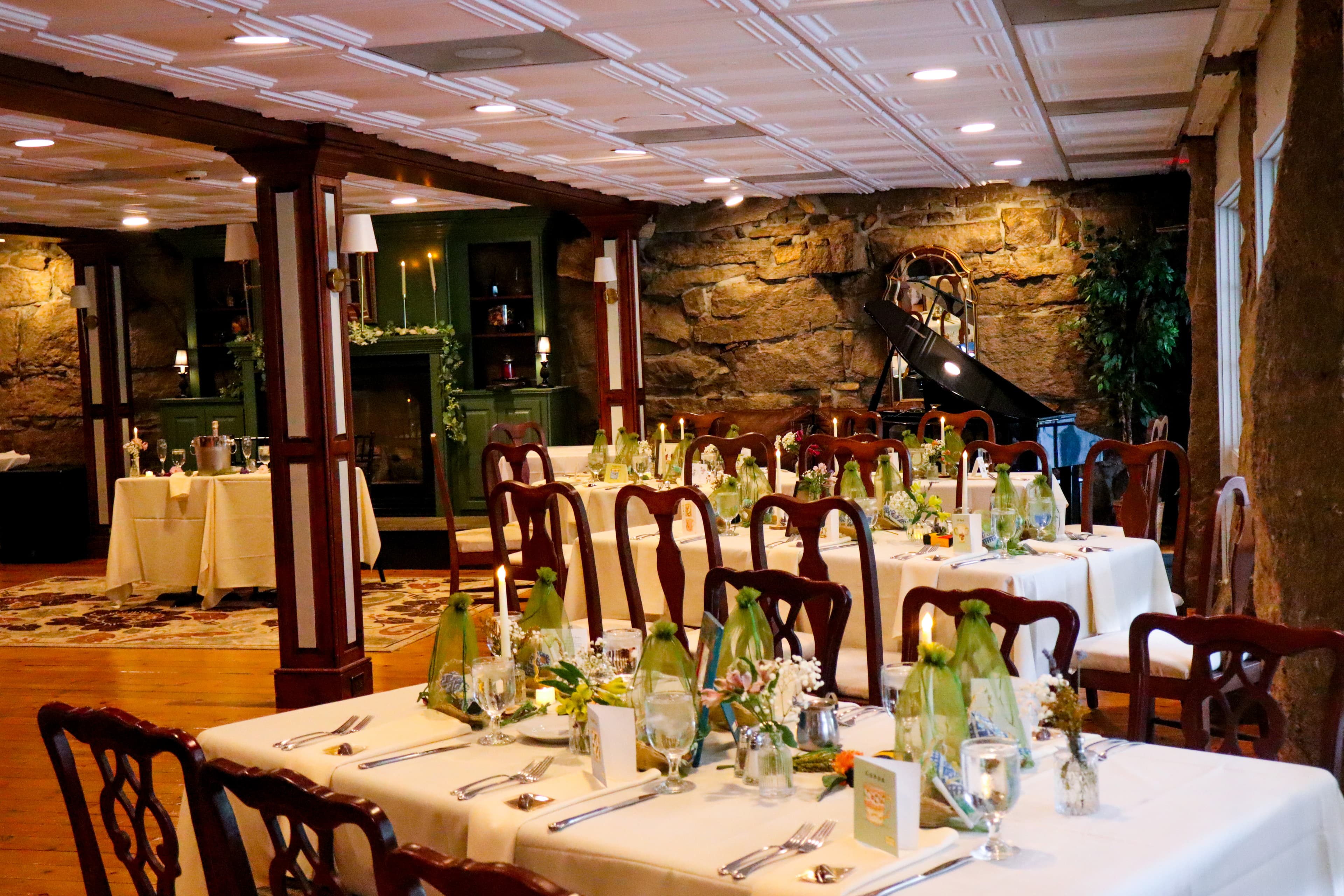 A beautifully set dining room with wooden furniture, elegant table settings, and a stone wall backdrop.