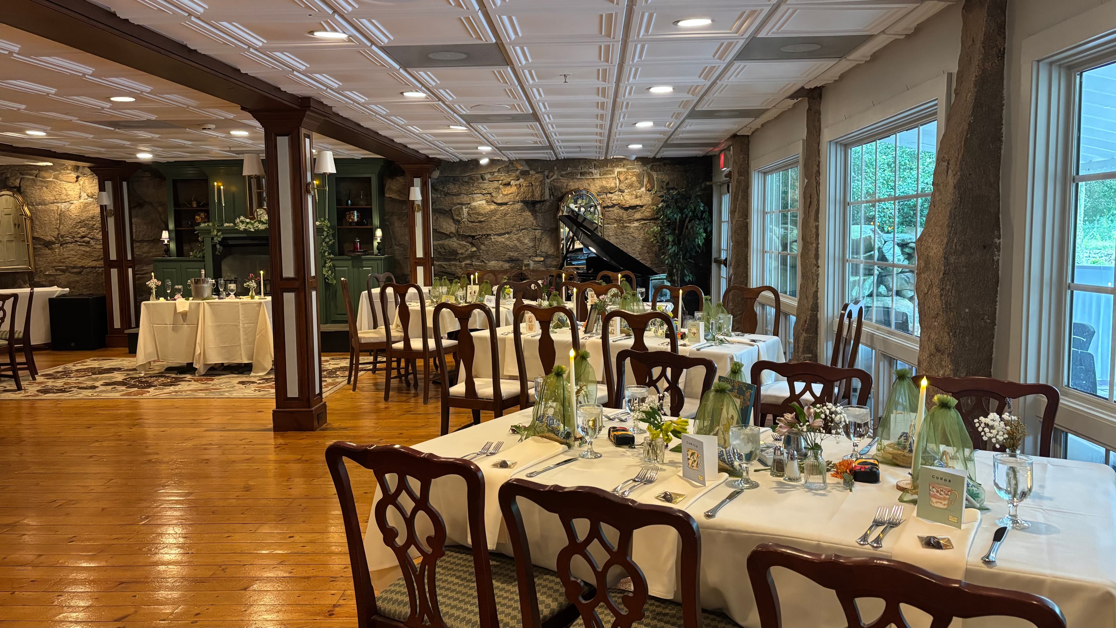 An elegantly set dining room featuring tables with white tablecloths, glassware, and a stone wall backdrop.