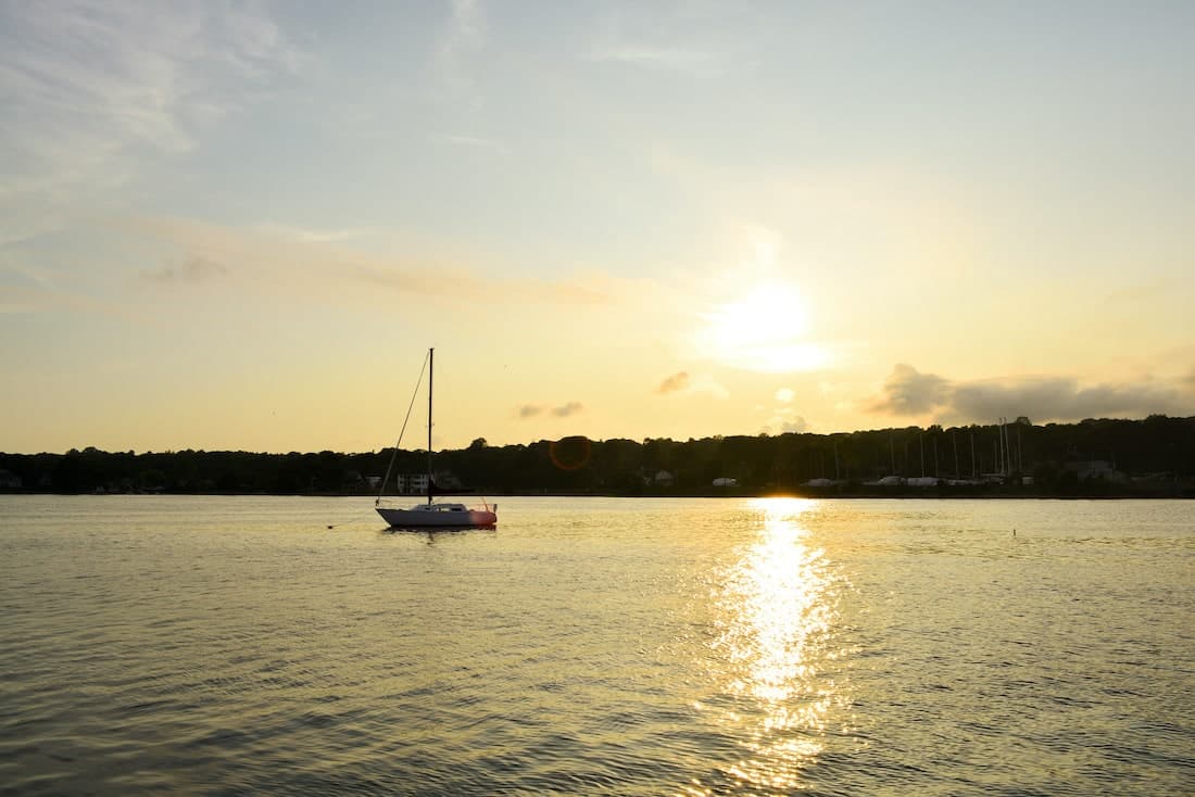 A sailboat is anchored on a calm waterway at sunset.