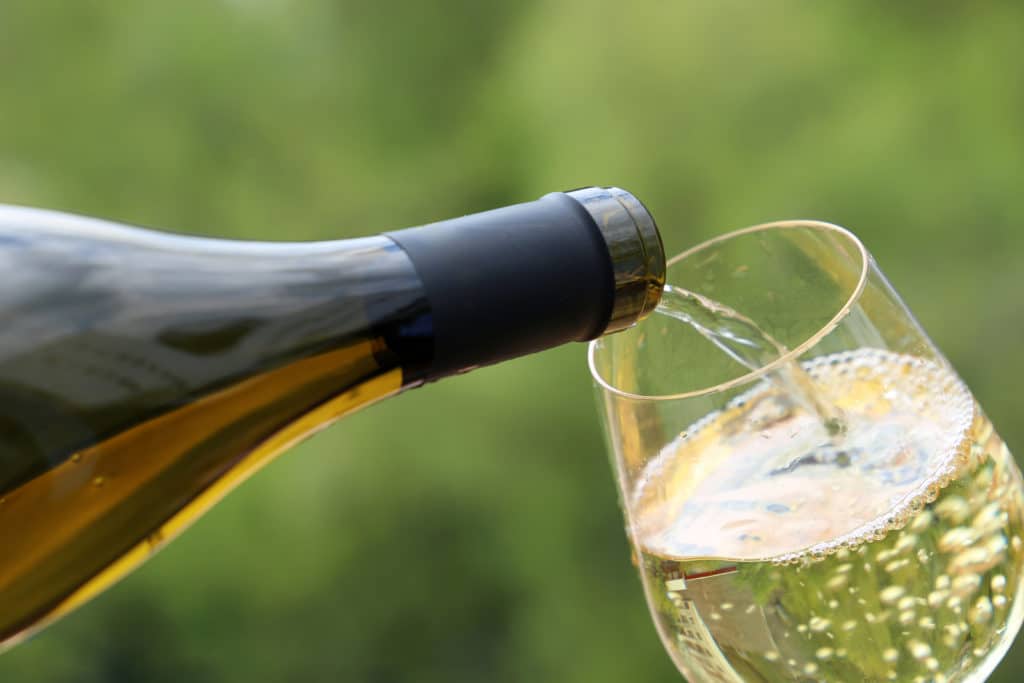 A bottle of white wine is pouring into a glass outdoors.