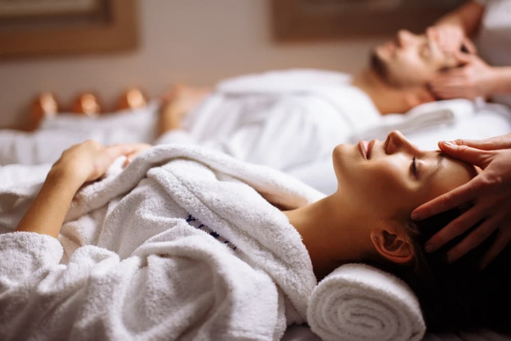 A woman receives a facial massage while a man relaxes beside her in a spa setting.