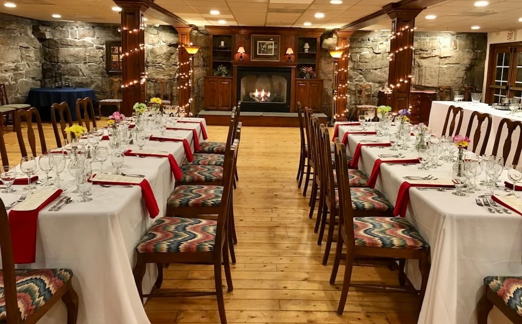 Elegant dining setup with decorated tables, glassware, and a cozy fireplace ambiance.