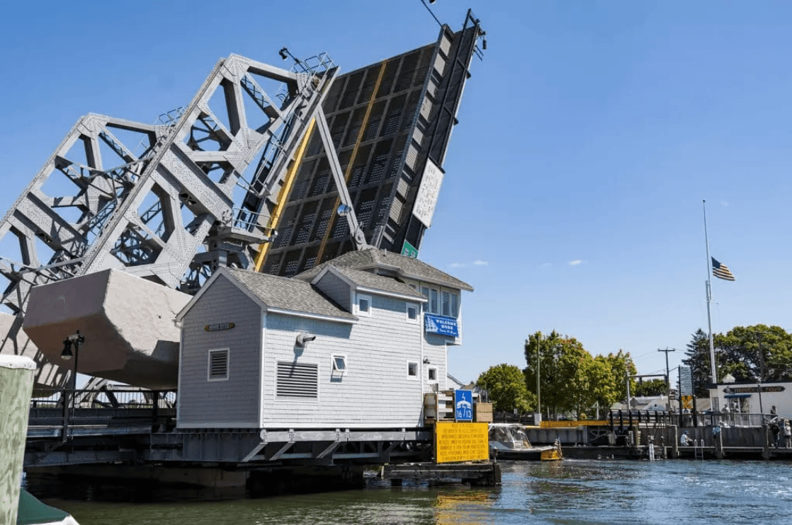 A bascule bridge is raised next to a small house on the water's edge.