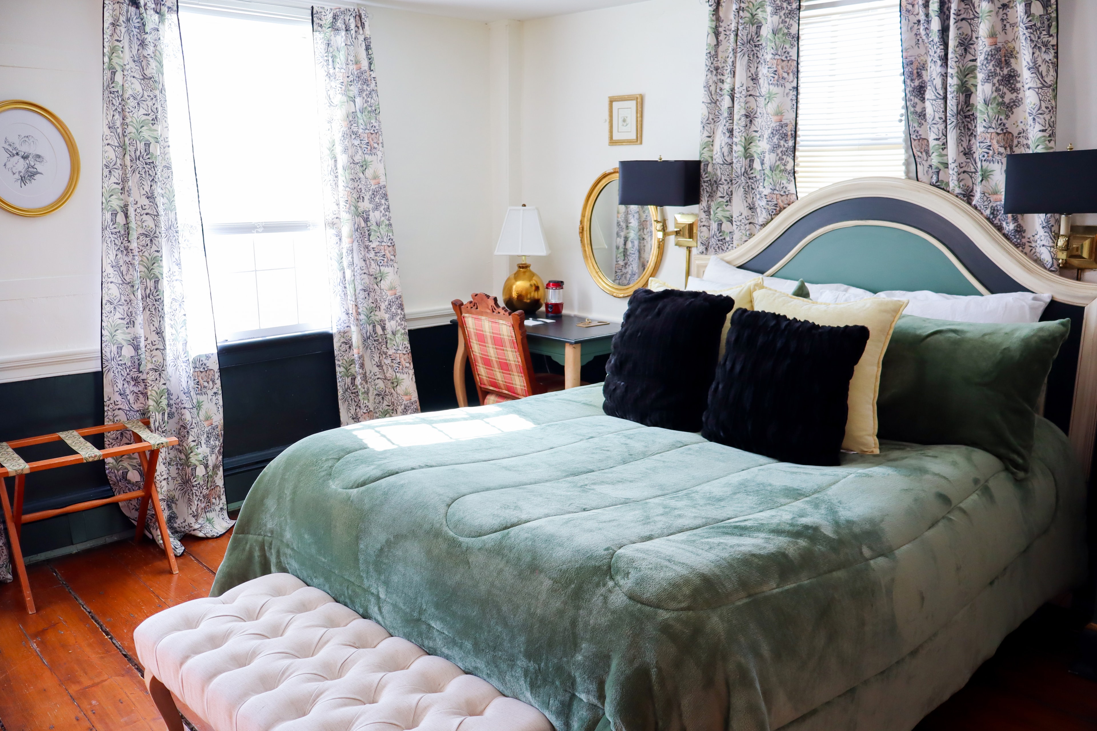 A romantic bedroom featuring a large white bed, vintage patterned wallpaper, a teal dresser, and a light wood wardrobe with a robe hanging nearby.
