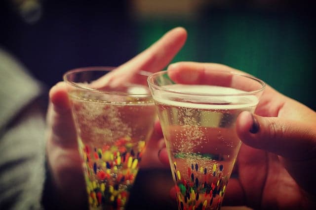 Two hands clinking glasses filled with sparkling drink and colorful candies.