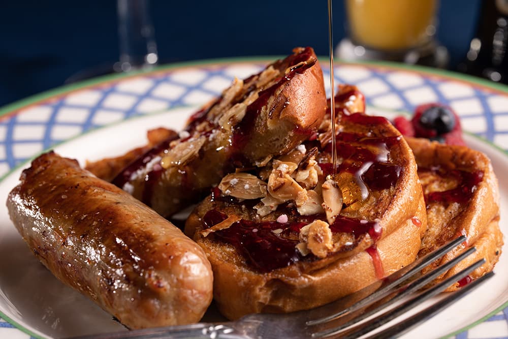 A plate of French toast topped with syrup, almonds, and a side of sausage.