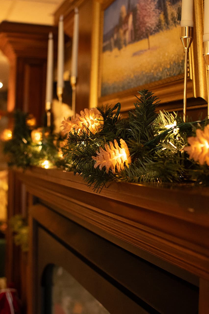 A decorated mantel with pine garland, glowing lights, and candles.