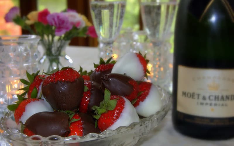 A dish of chocolate and white chocolate-dipped strawberries beside a bottle of Moët & Chandon champagne.