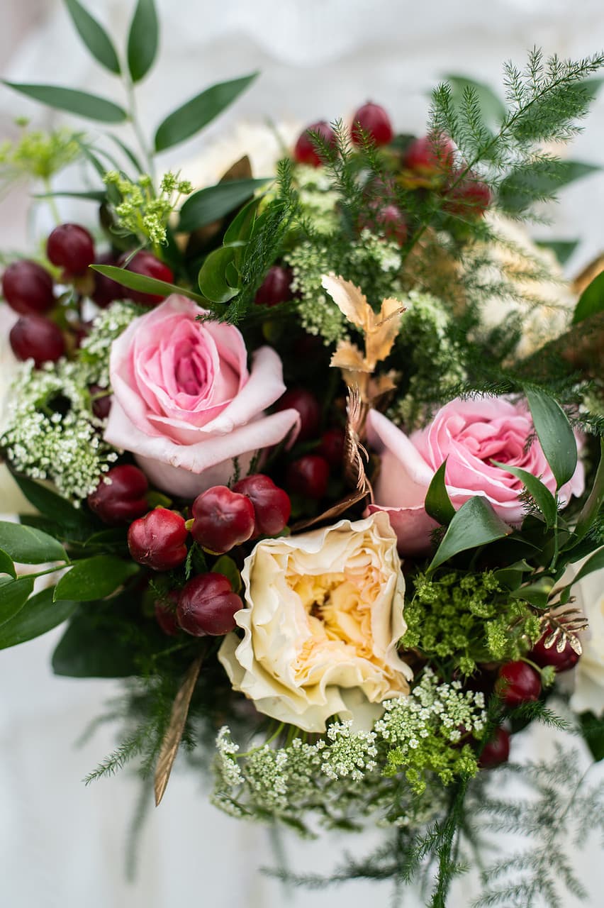 A close-up of a vibrant bouquet featuring pink and yellow roses, green foliage, and red berries.