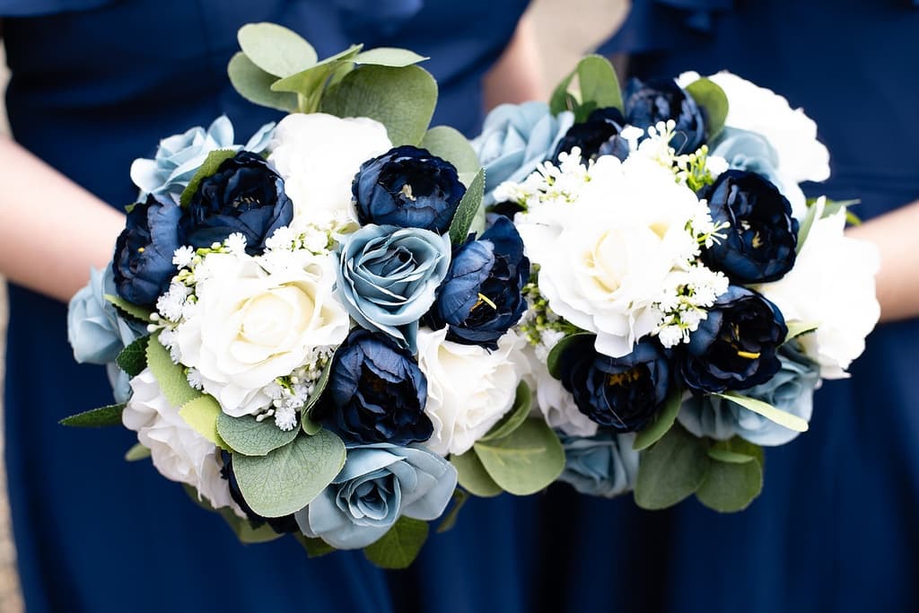 Two bridesmaids hold elegant bouquets featuring navy, white, and light blue flowers.