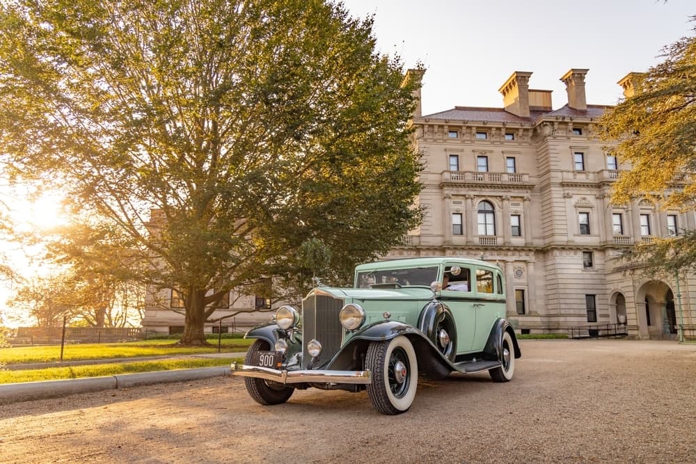 A vintage green car parked in front of a grand, historic building during sunset.