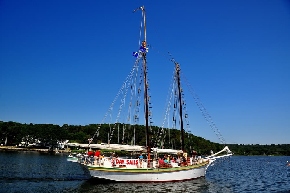 A sailing vessel with passengers moves through a calm harbor under a clear blue sky.