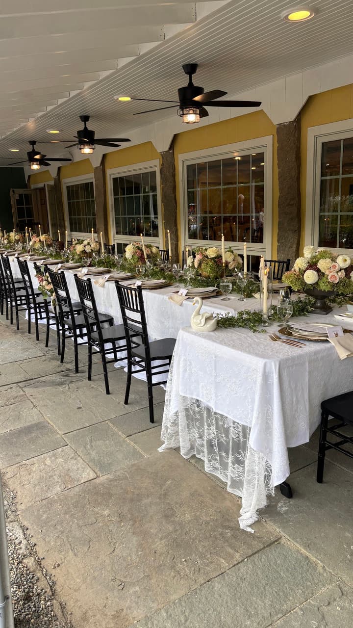A beautifully arranged outdoor dining table with white lace tablecloths, floral centerpieces, and candleholders.