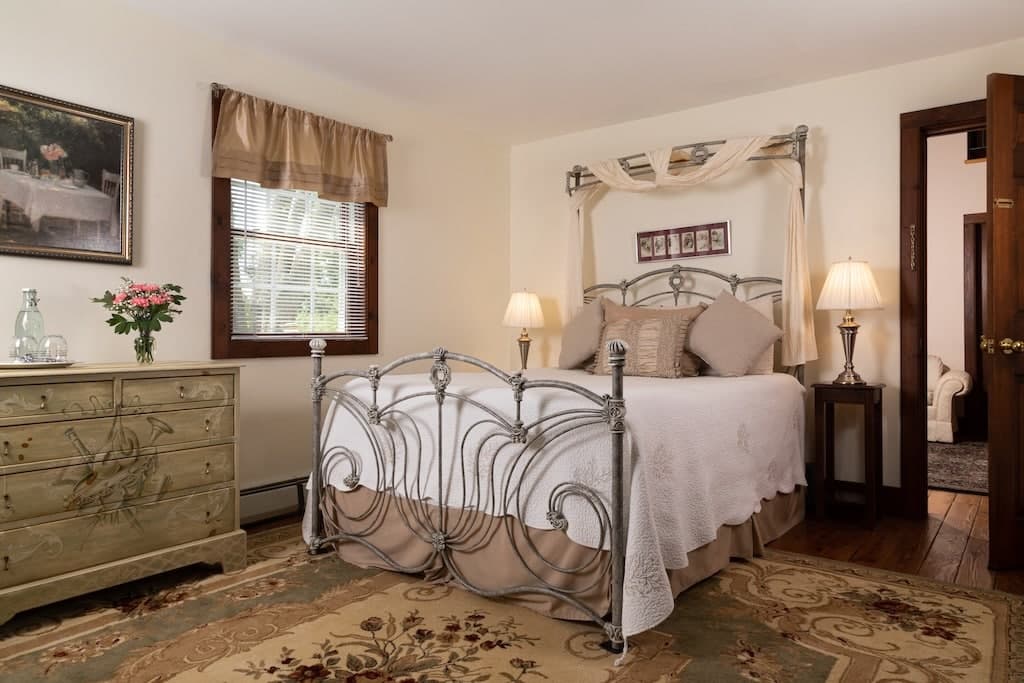 A cozy bedroom featuring a metal bed frame, soft bedding, and a wooden dresser with flowers.