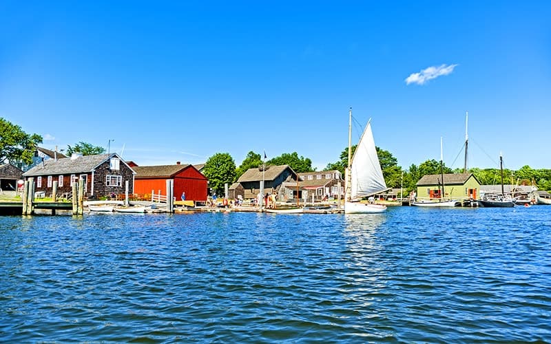 A calm harbor scene featuring colorful buildings and a sailboat on blue water under a clear sky.