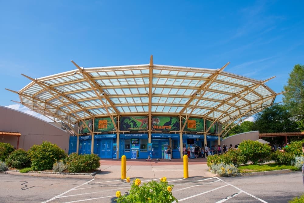 Entrance to a dinosaur-themed attraction with a large, transparent roof and landscaped gardens.