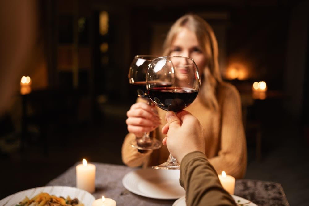 Two individuals toast with glasses of red wine at a candlelit dinner.