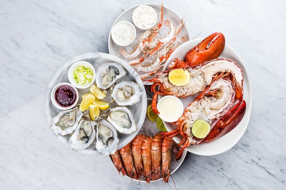 A platter of fresh seafood including lobster, shrimp, and oysters with dipping sauces and lemon slices.
