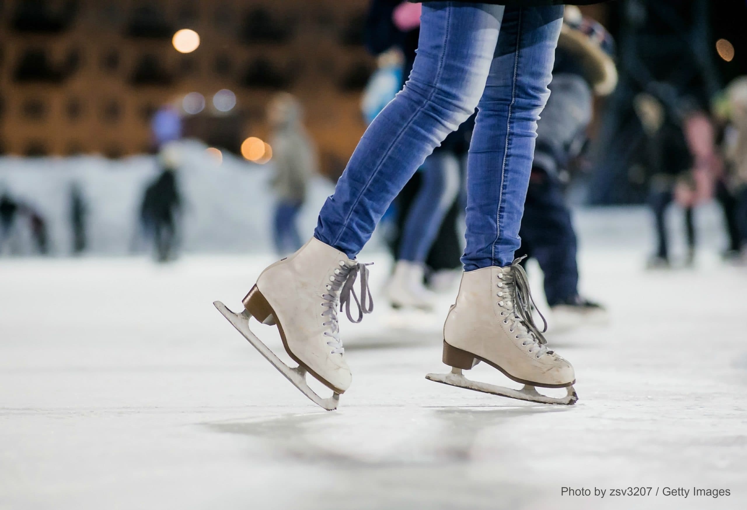 A pair of ice skates gliding on a rink with blurred figures in the background.