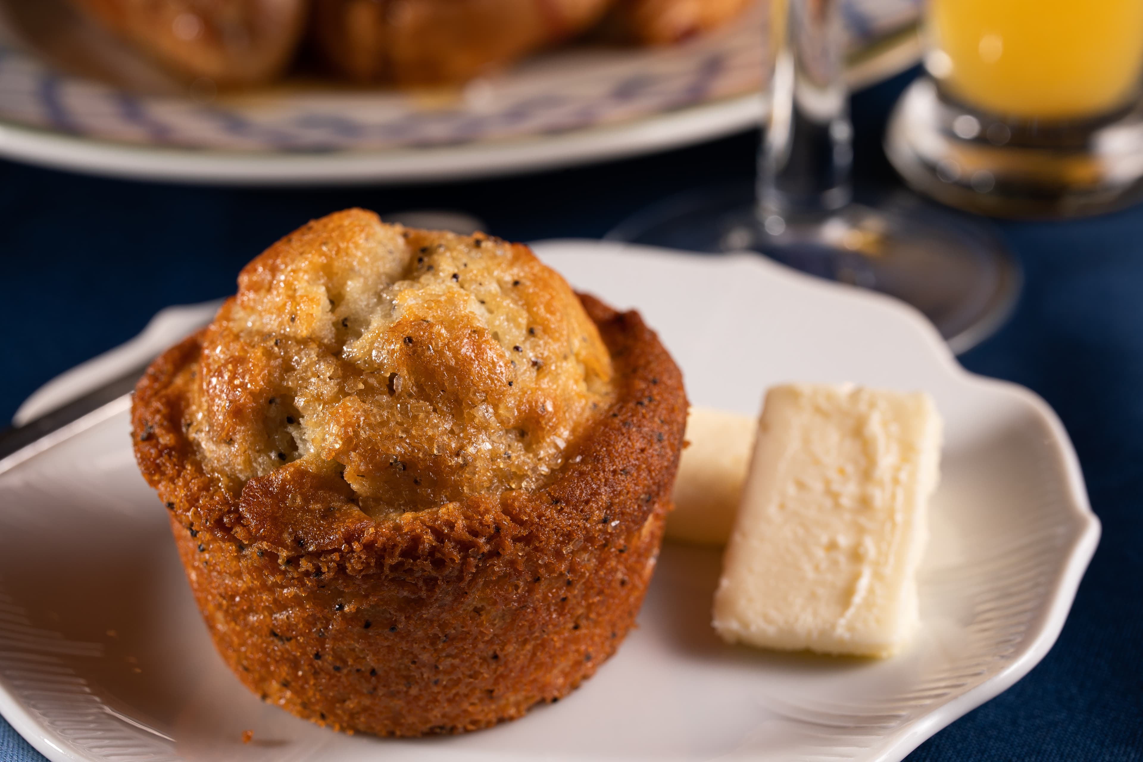 A golden muffin with a crusty exterior sits on a plate next to two slices of butter.