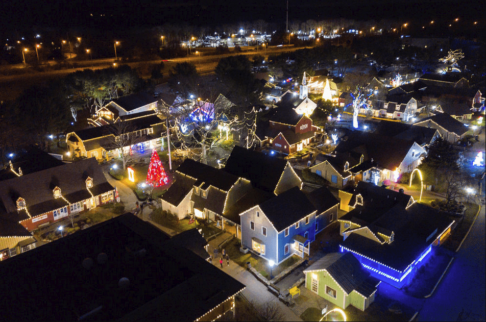 Aerial view of a neighborhood beautifully decorated with colorful Christmas lights and a lit tree at night.