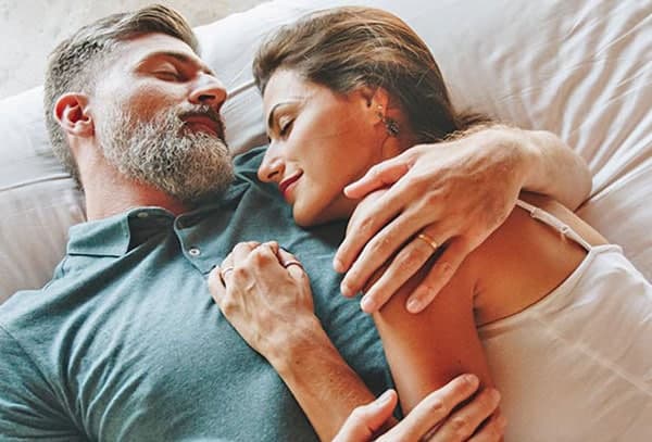 A couple peacefully embraces while lying on a bed, expressing intimacy and affection.