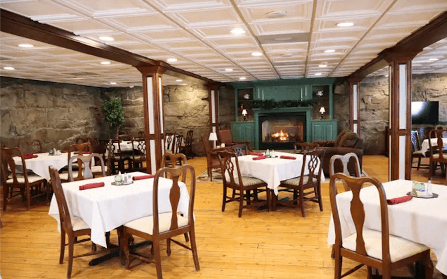 Cozy restaurant interior featuring wood-paneled columns, tables dressed in white cloths, and a fireplace.