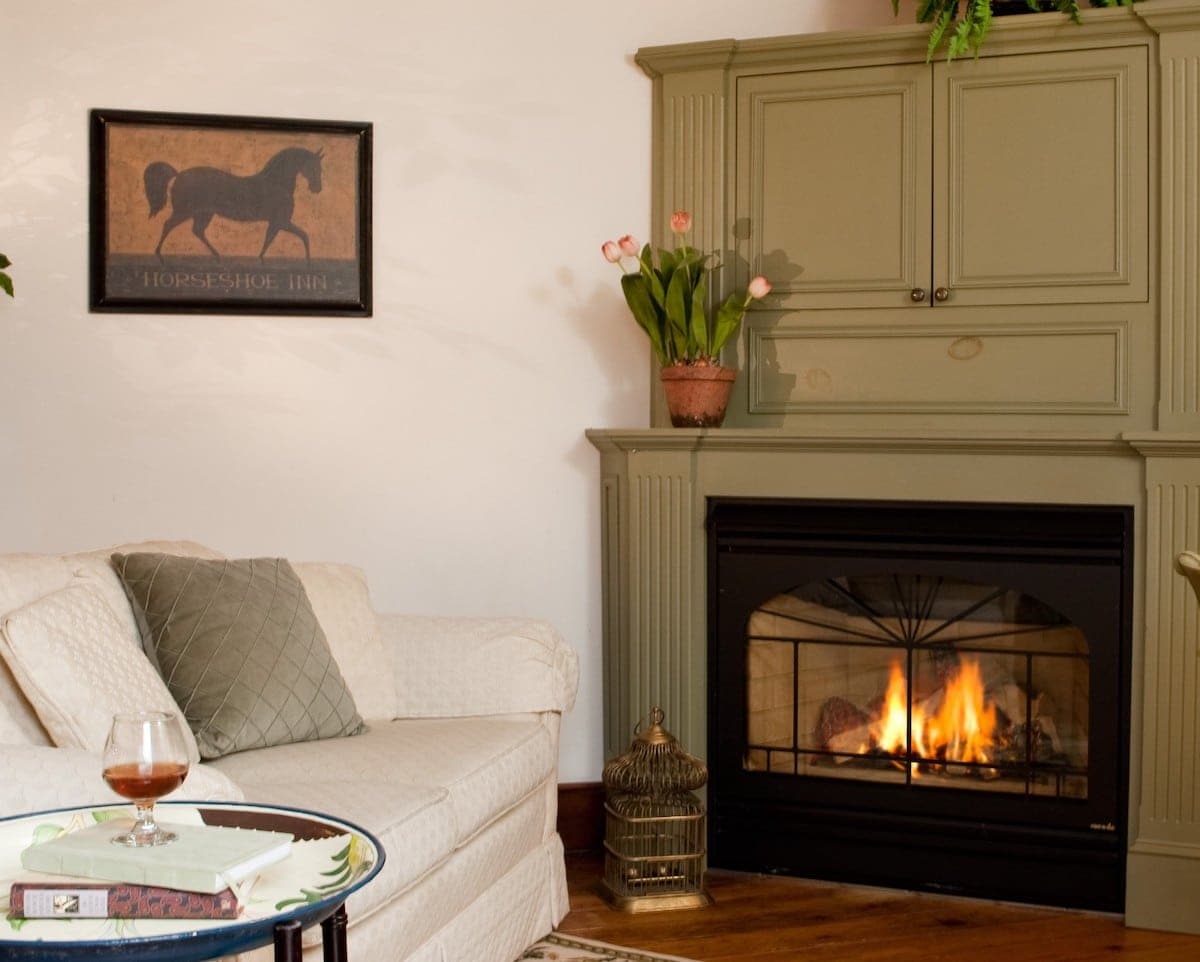 Cozy living room featuring a white sofa, a glass of drink on a table, a fireplace, and a horse-themed painting.