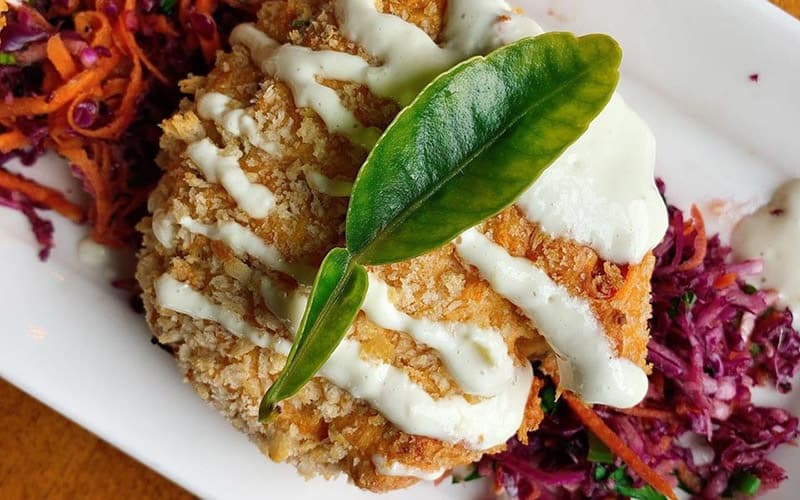 A crispy fried dish topped with a green leaf, served alongside colorful slaw.