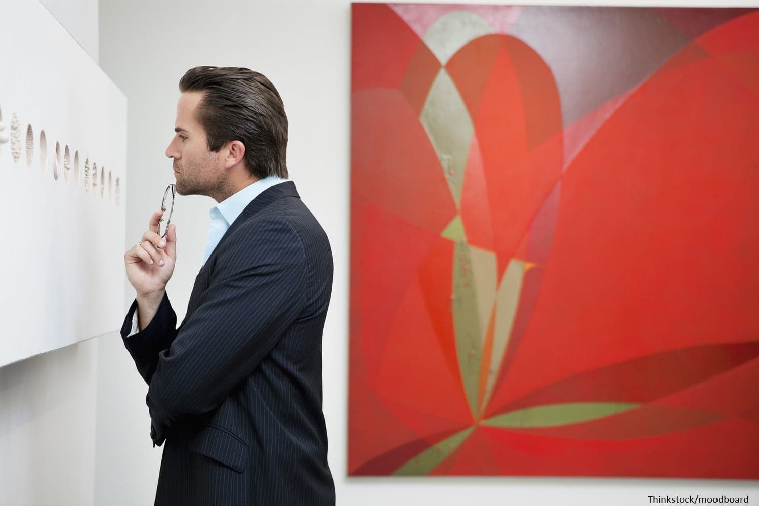 A man in a suit thoughtfully examines artwork in a gallery.