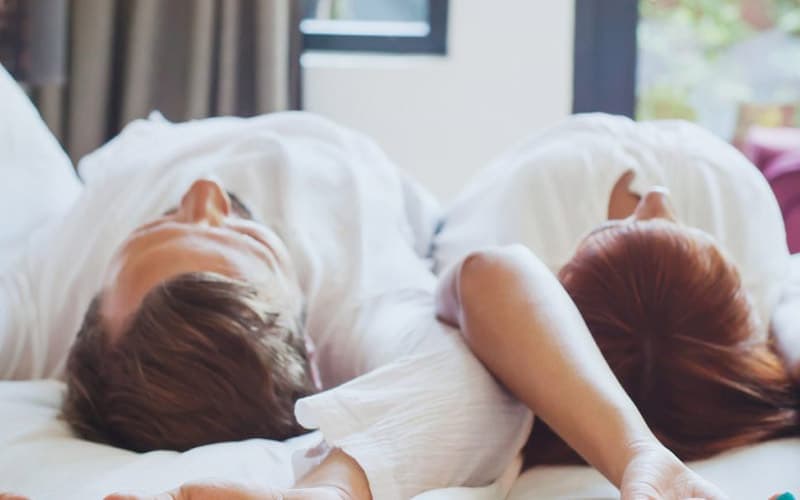 A couple lying back to back on a bed, relaxed and comfortable.