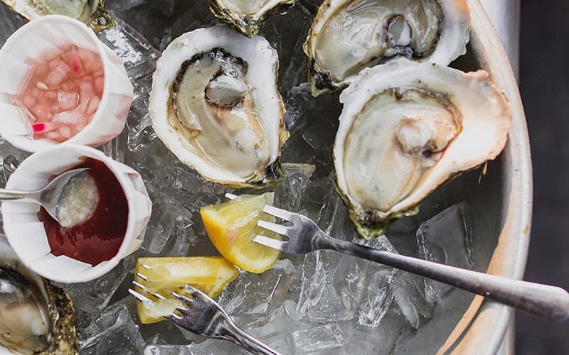 A platter of fresh oysters served on ice with lemon wedges and sauces.