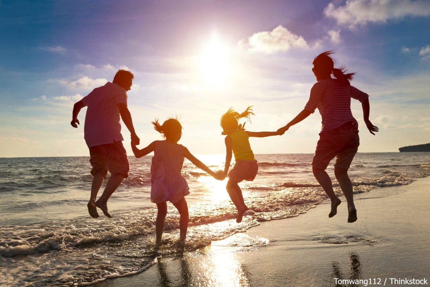 A family of four joyfully jumps in the shallow water at the beach during sunset.