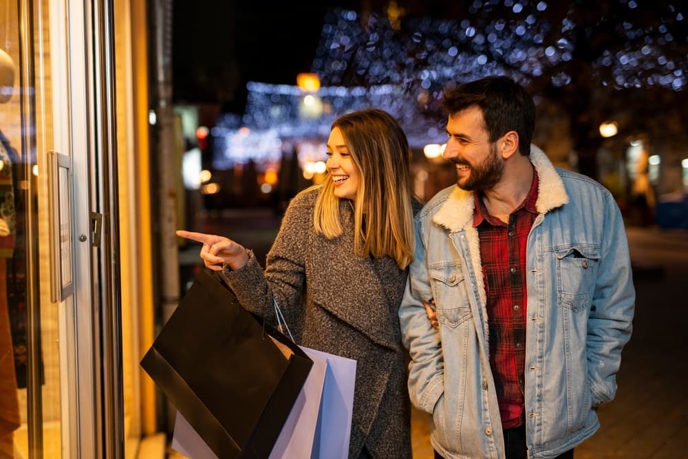 A couple enjoys shopping together while admiring a store window display at night.