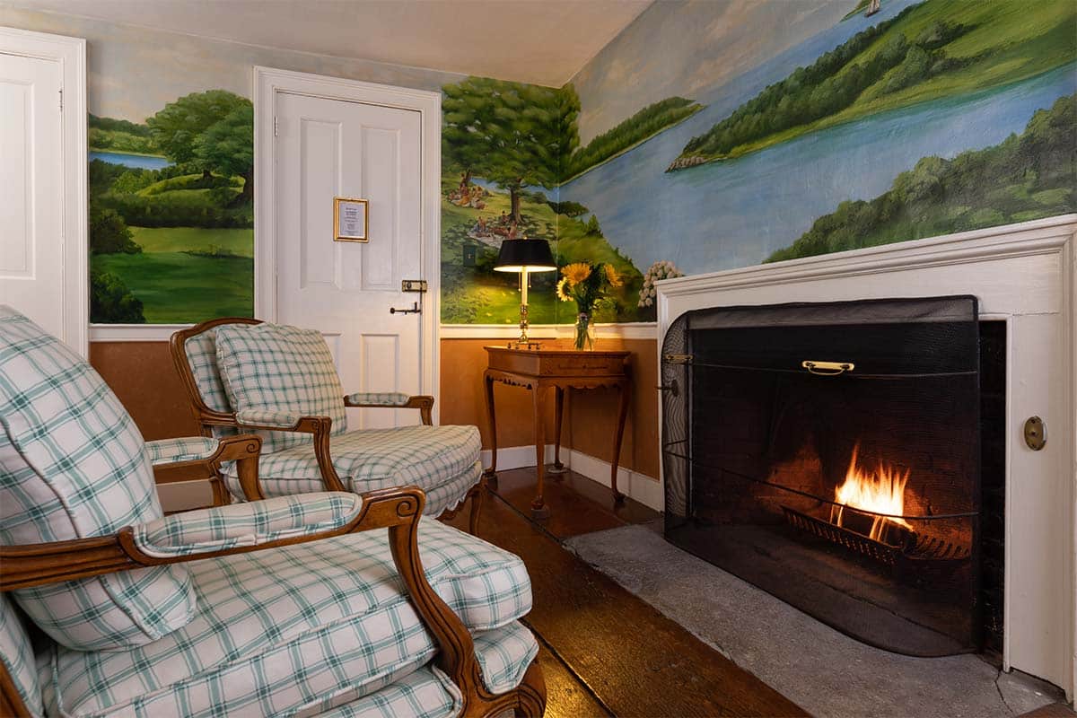 Cozy living room featuring plaid armchairs, a wooden side table, and a fireplace with a warm glow.