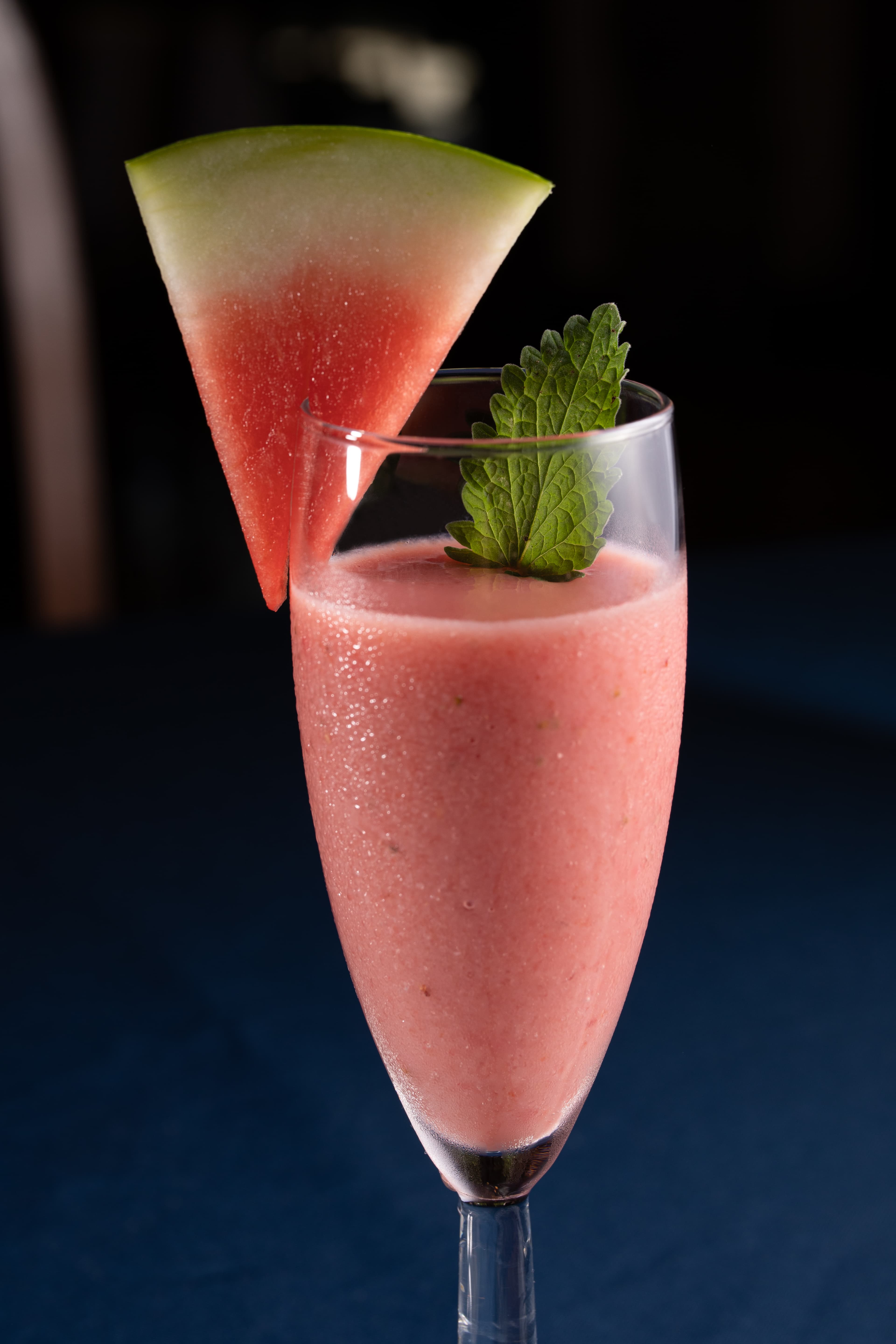 A frosty pink watermelon cocktail garnished with a mint leaf and a watermelon slice.