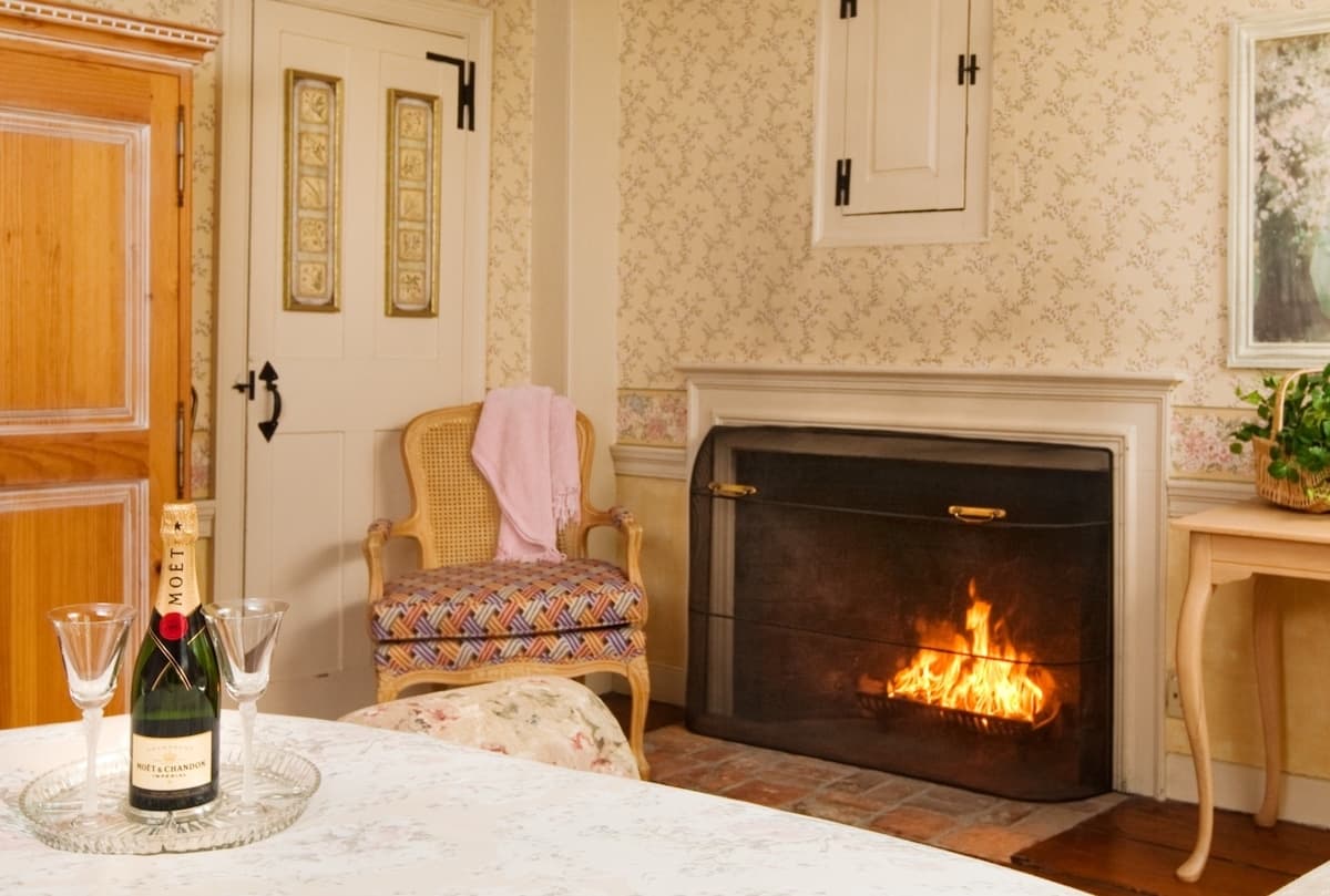 A cozy living room featuring a fireplace, a bottle of champagne with glasses, and a patterned chair.