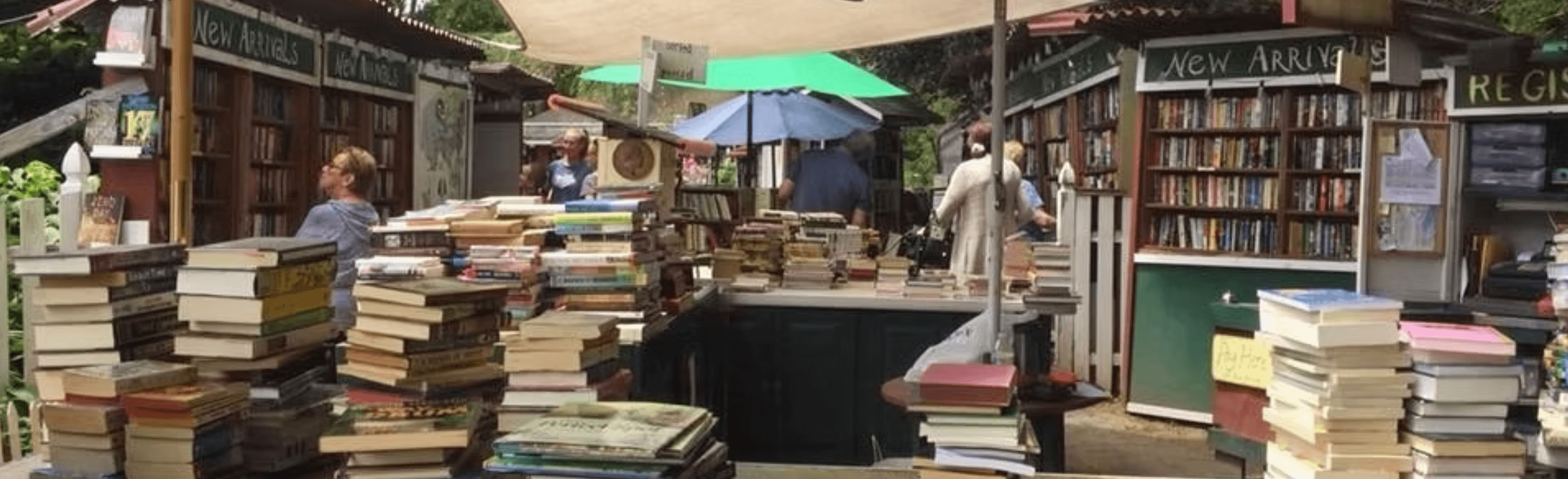 A bustling outdoor book market with stacks of books and shaded areas for browsing.
