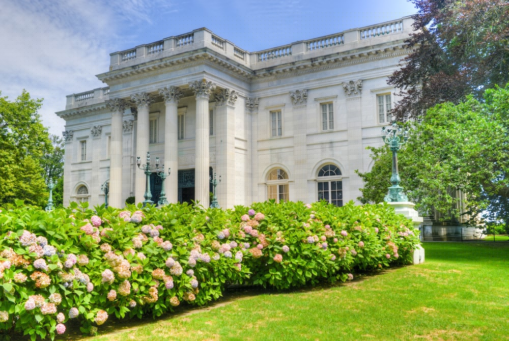 A grand white mansion surrounded by blooming hydrangea bushes under a blue sky.