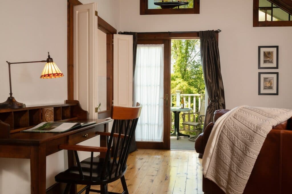 A cozy interior featuring a wooden desk, chair, and doorway leading to a balcony with natural light streaming in.