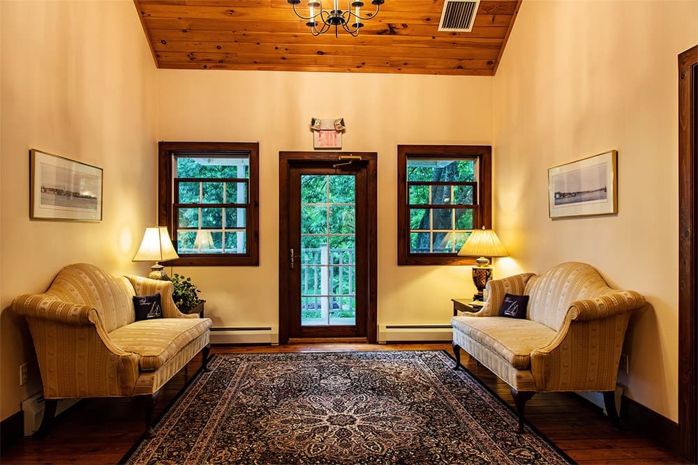 A cozy entryway featuring two upholstered sofas, a decorative rug, and large windows leading out to a porch.